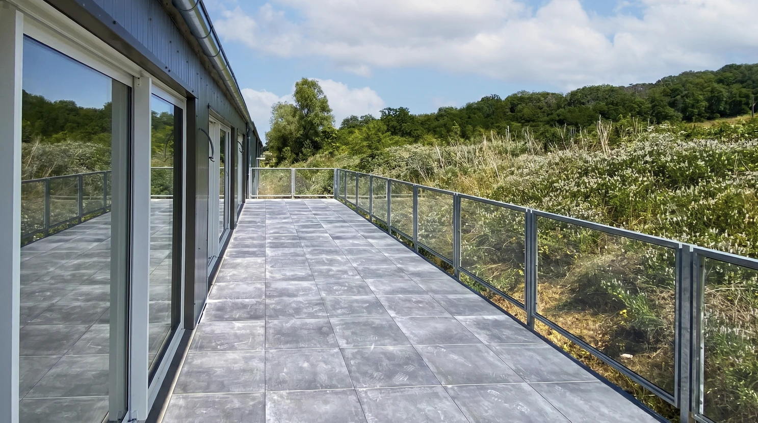 Terrasse extérieure moderne longeant un bâtiment contemporain à bardage métallique bleu-gris