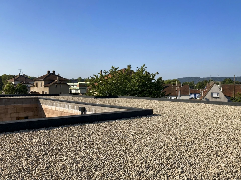 Ouvrier en tenue de travail appliquant un revêtement d'étanchéité sur une terrasse extérieure à l'aide d'un chalumeau à gaz